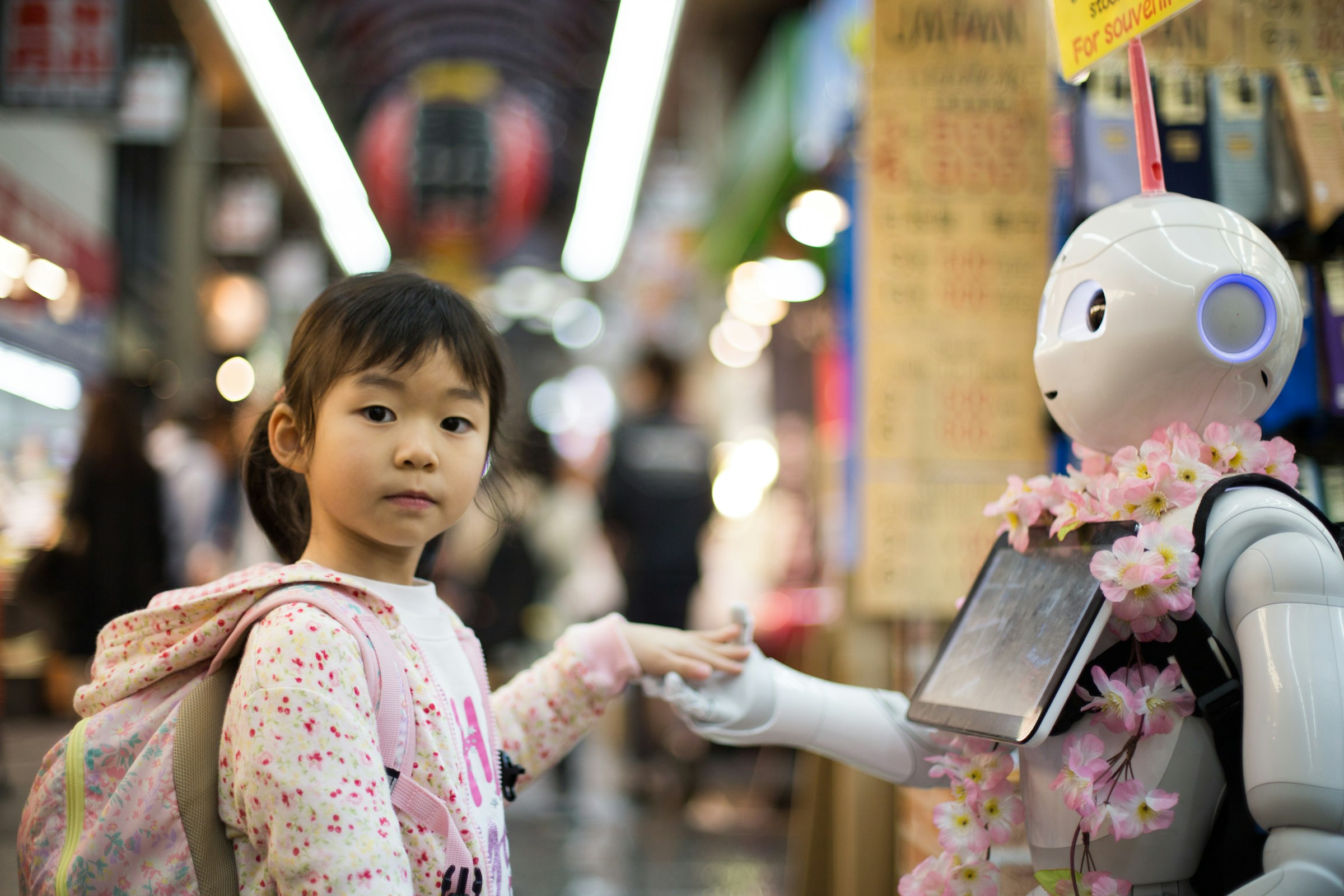 A child reaches out to a humanoid robot in a market street